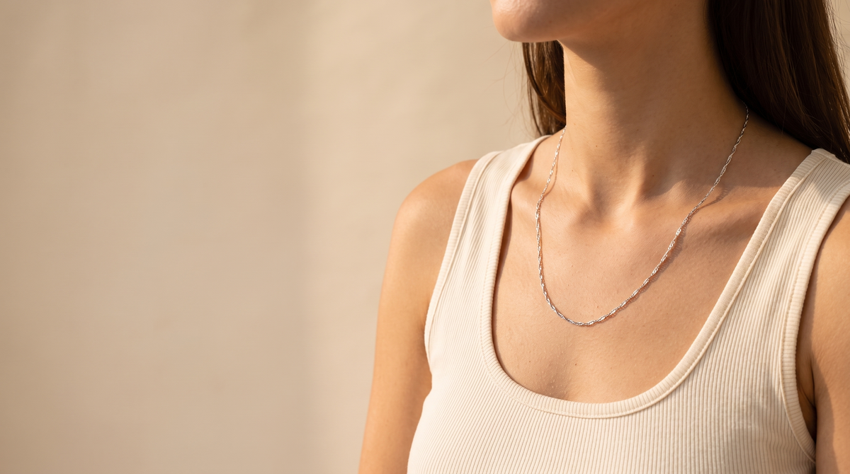Fine silver chain necklace worn at the collarbone in soft daylight