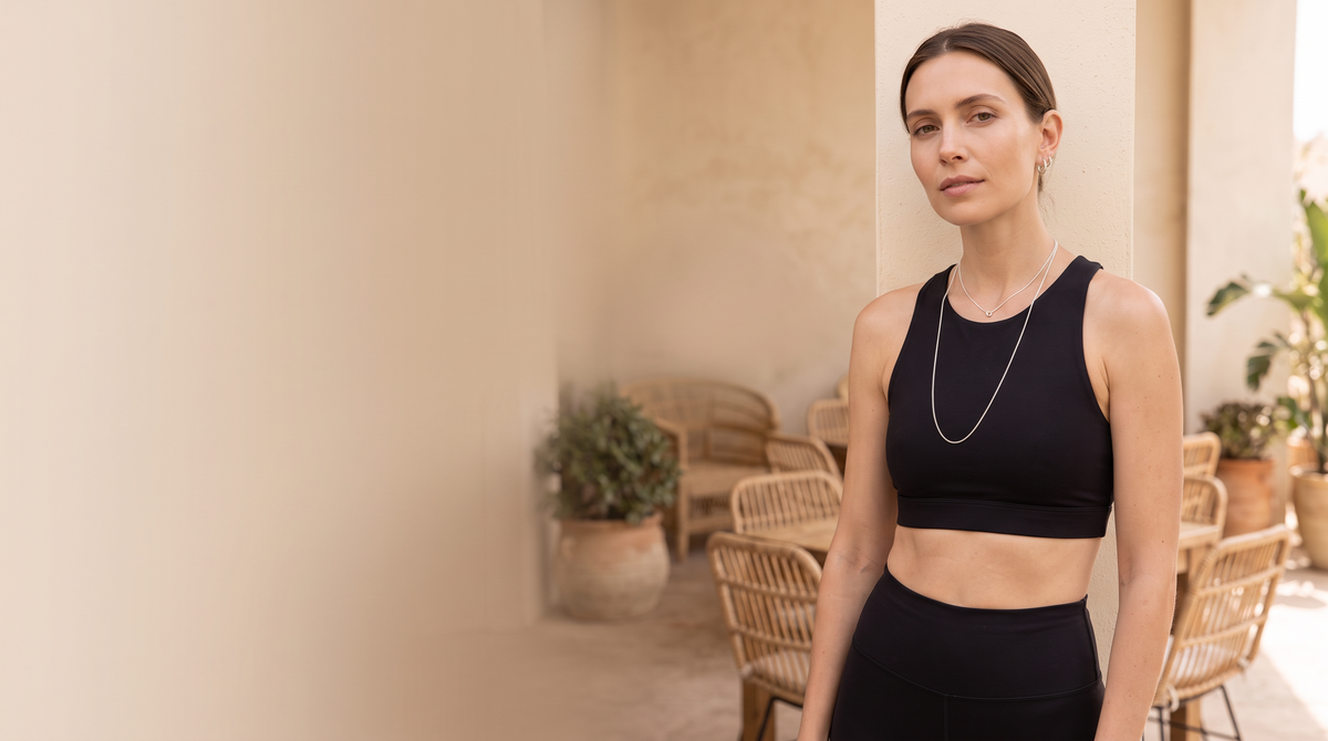 Woman in black activewear wearing layered chain necklaces against a warm neutral wall