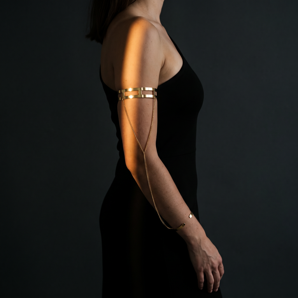 Delphine gold arm and wrist chain cuff worn with a black one-shoulder dress