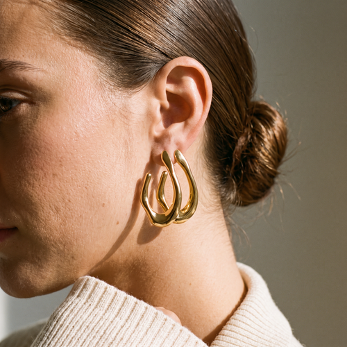 Amara sculpted gold hoop earring worn, close-up in soft window light