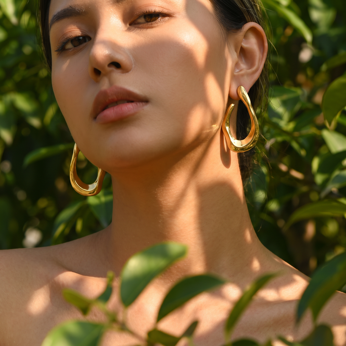 Amara sculpted gold hoop worn in dappled sunlight