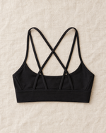 Orla Lattice Back Sports Bra in black laid flat on cream linen