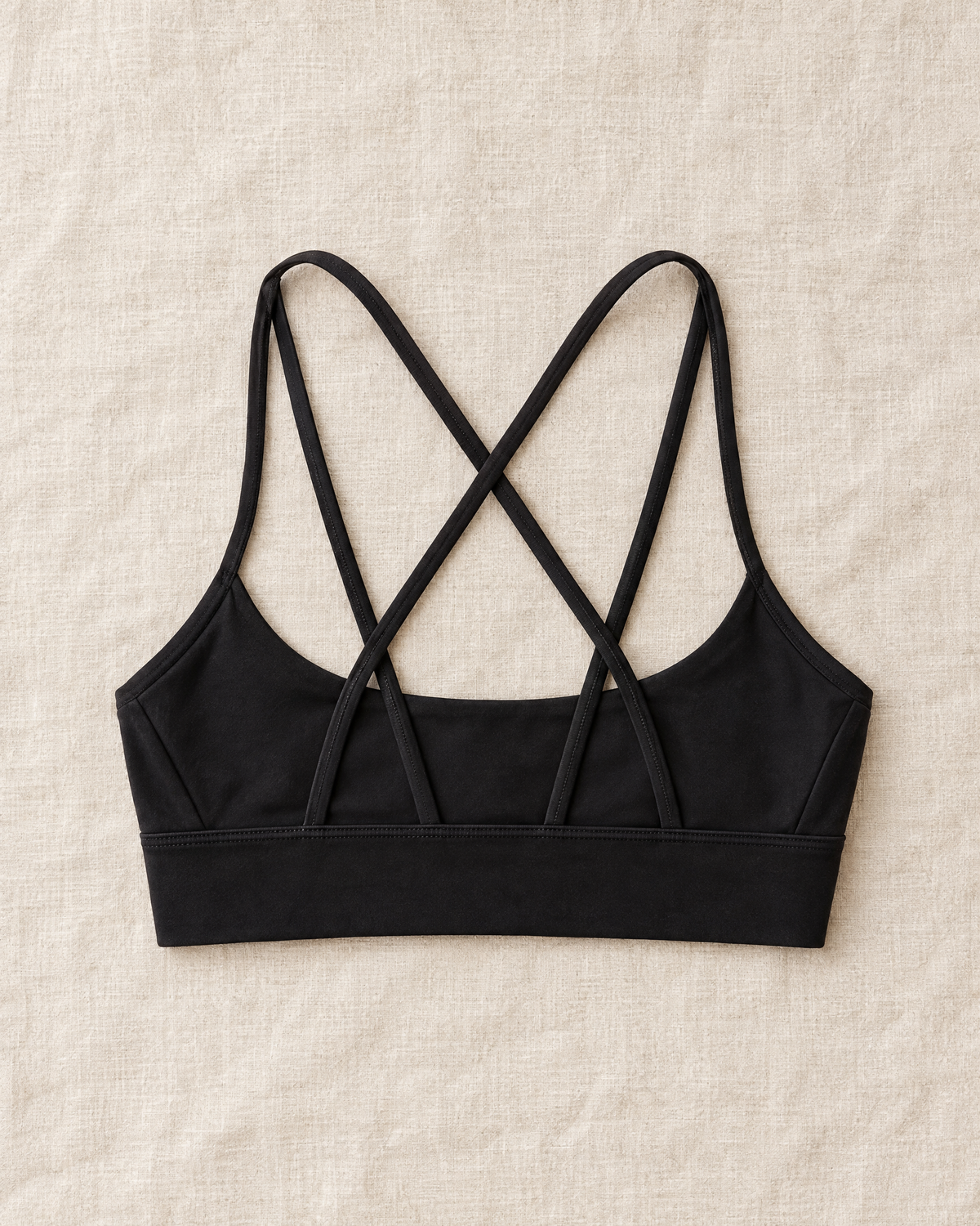 Orla Lattice Back Sports Bra in black laid flat on cream linen